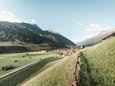 Deine Ferienwohnung in Neustift ✓ Dorf in einem grünen Tal mit Bergen und blauem Himmel