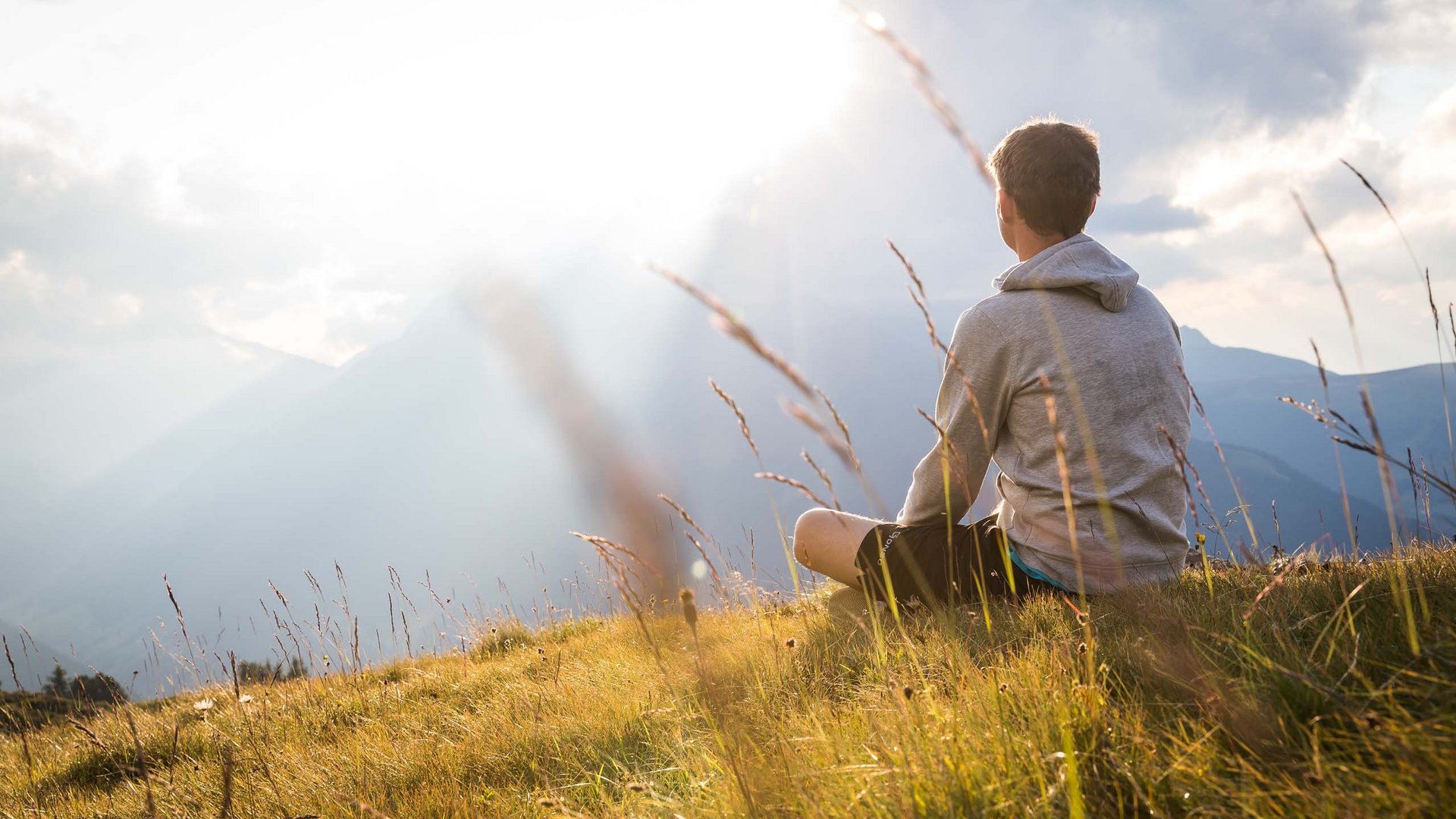 Beispielaufbau einer Unterseite Junger Mann sitzt auf Wiese und blickt auf Berge im Sonnenlicht