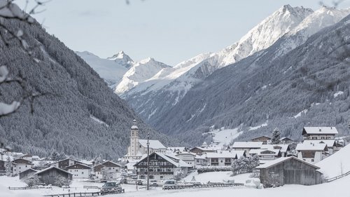 Non-binding enquiry: your apartment in Stubai ➔ Snowy mountain village with church tower and snow-covered Alps in background