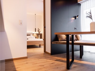 Ferienwohnung in Neustift im Stubaital mit Style ❥ Moderner Wohnbereich mit Holzboden, Bank, Tisch und Blick ins Schlafzimmer
