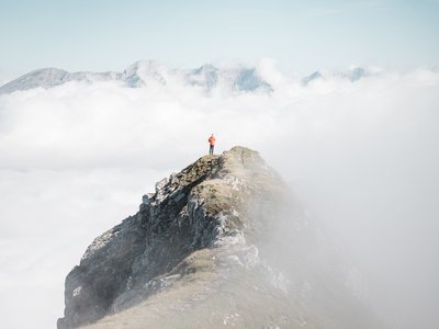 Unterkunft in Neustift im Stubaital: die beste Lage ⬤ Person steht auf einem Berggipfel über den Wolken umgeben von Nebel