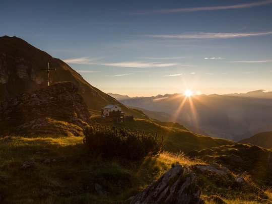 Beispielaufbau einer Unterseite Sonnenuntergang über Bergen mit einer Hütte und einem Gipfelkreuz im Vordergrund