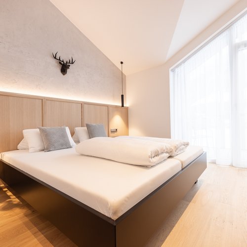 Your holiday apartment in Neustift ✓ Modern bedroom with large bed, wooden floor, and large window with curtains