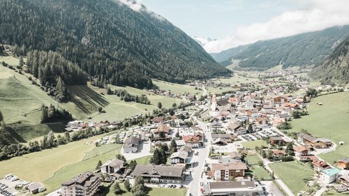 Unterkunft in Neustift im Stubaital: die beste Lage ⬤ Blick auf ein Dorf in einem grünen Tal zwischen bewaldeten Bergen